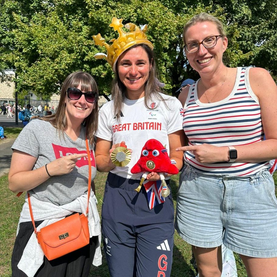 Three women celebrate together, one wearing a crown and holding a plush toy, smiling.